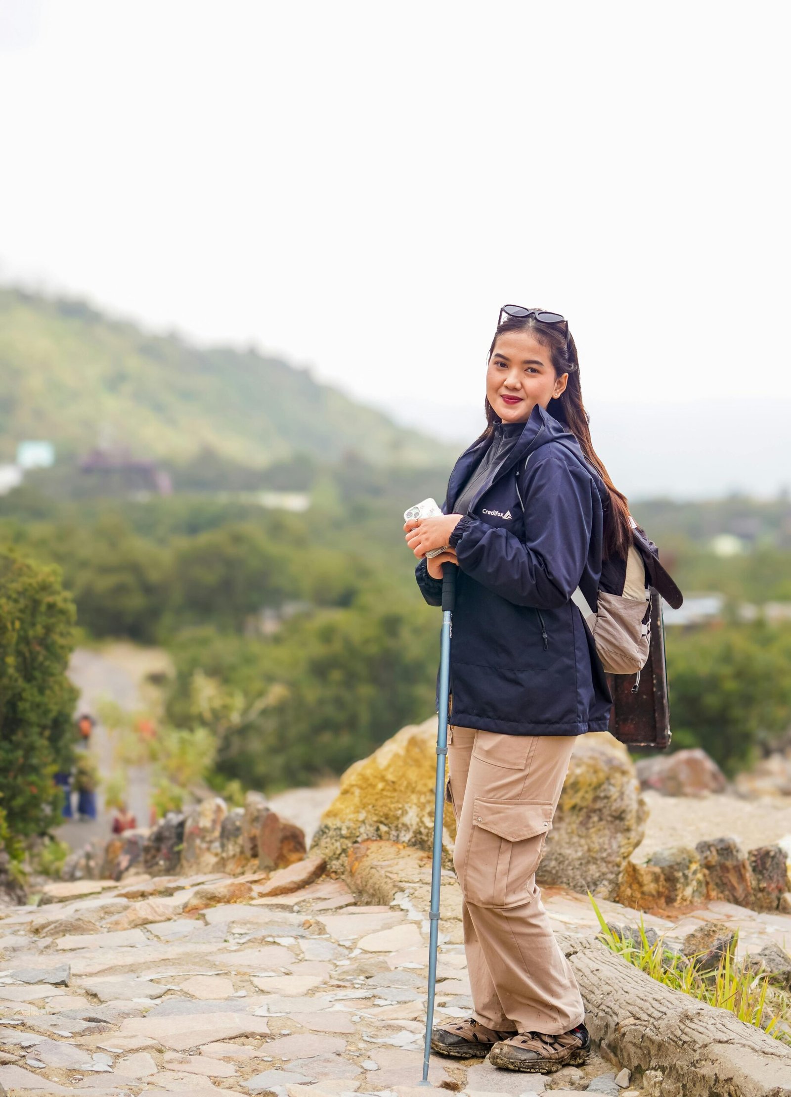 Woman hiking in scenic West Java, Indonesia with trekking pole and backpack, embracing adventure.
